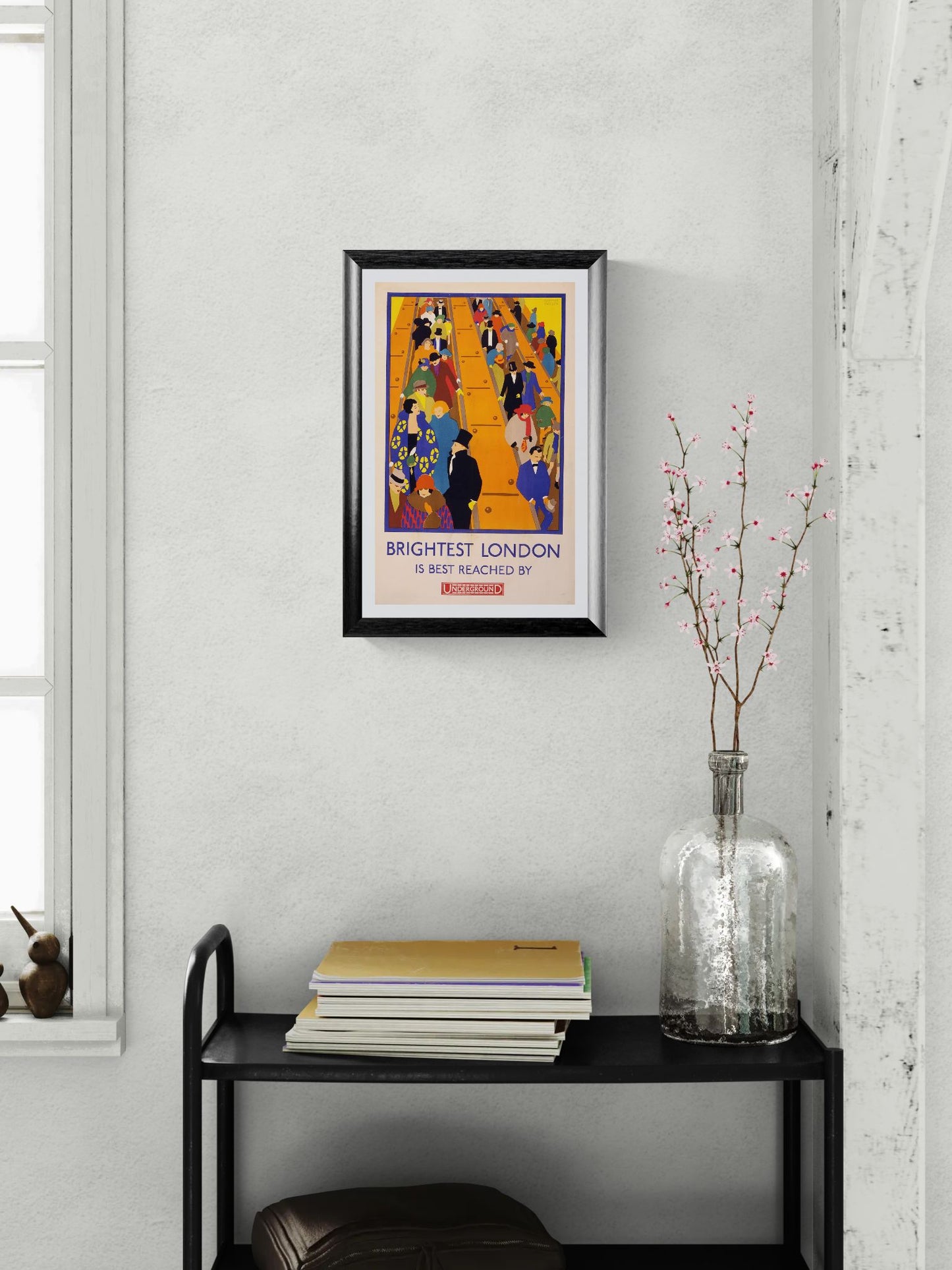 Framed poster on a wall above a black shelf with books and a vase.