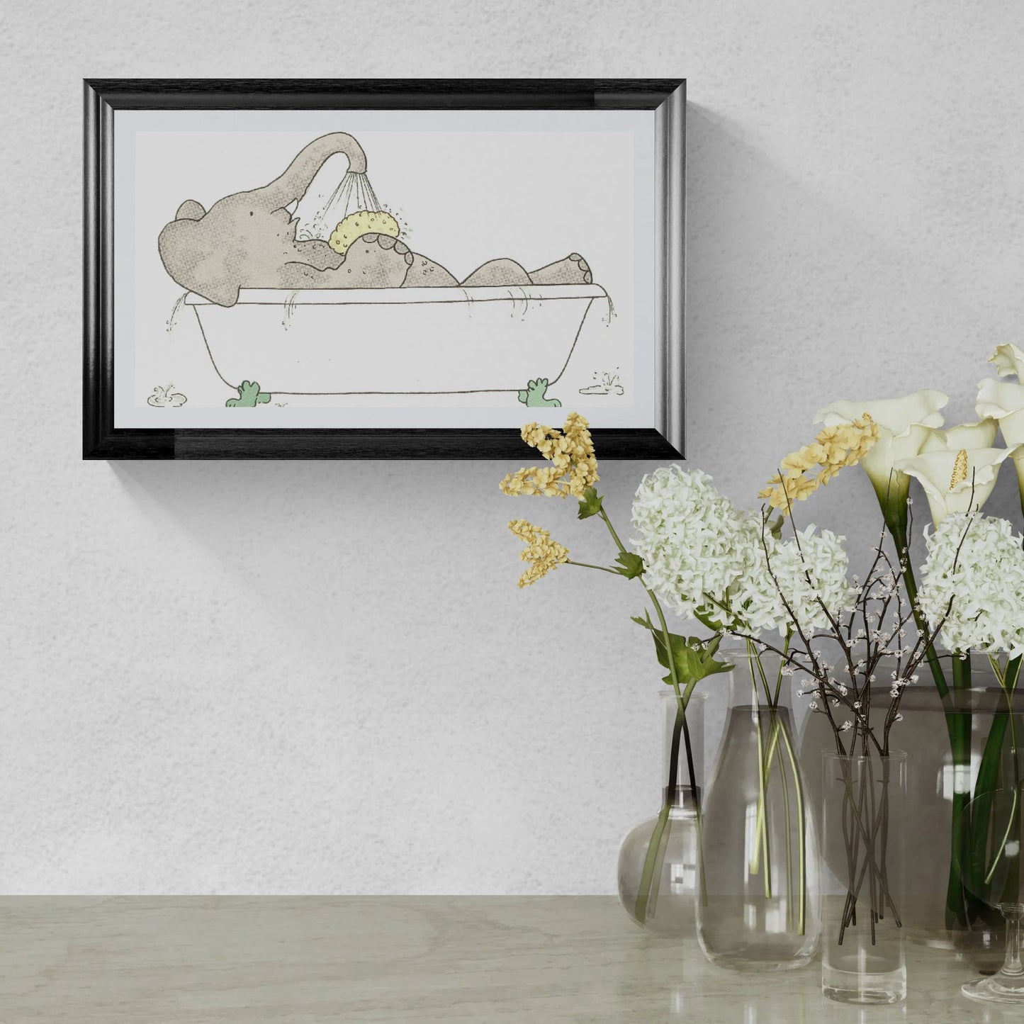 Framed illustration of an elephant taking a bath on a wall above a table with flowers.