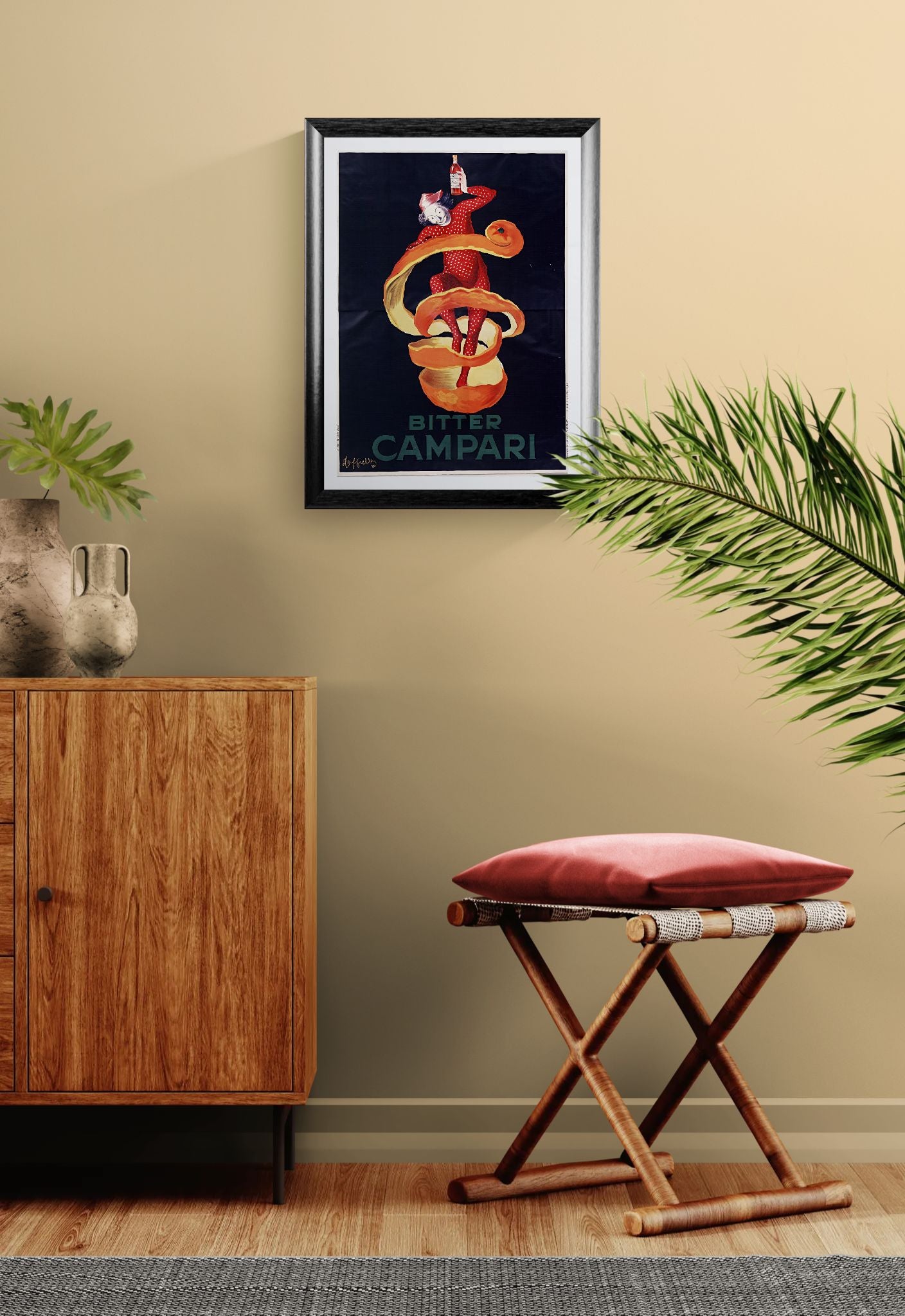 Framed artwork on a wall above a wooden cabinet with a red stool and plant in the foreground.