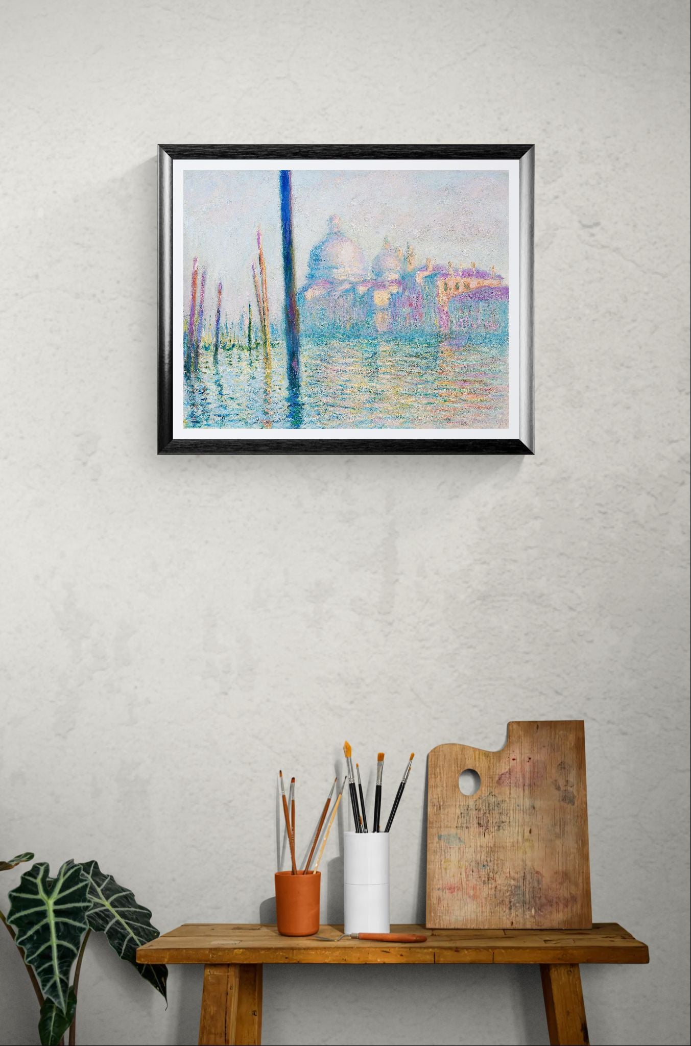 Framed Monet Venice artwork on a wall above a wooden table with art supplies.