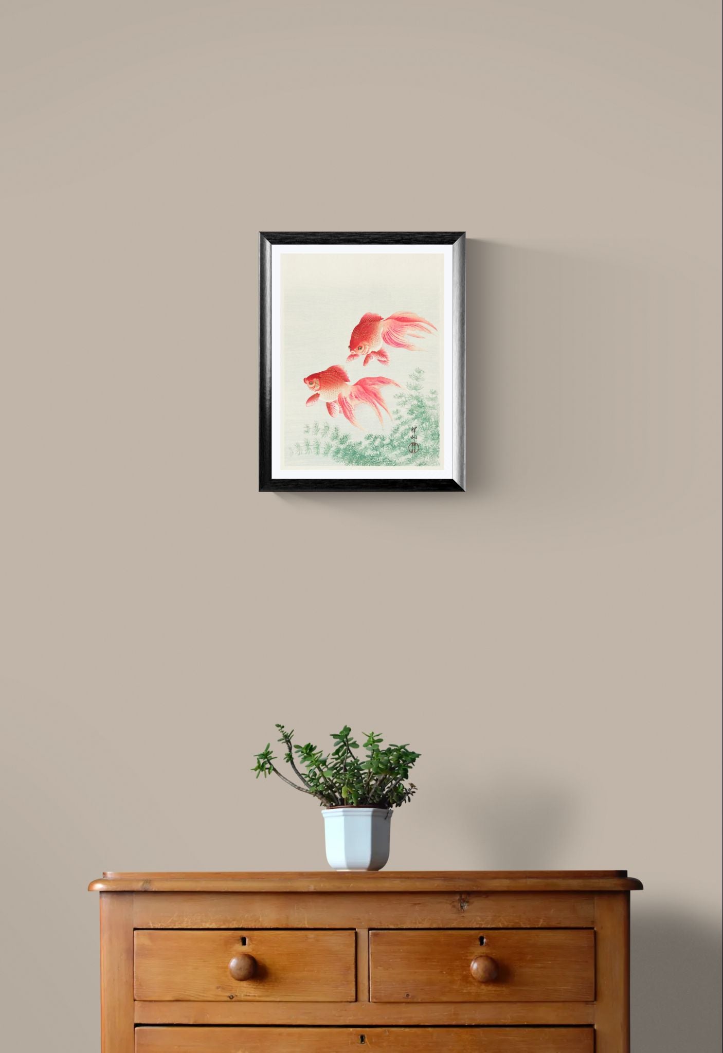 Framed artwork of two fish on a beige wall above a wooden dresser with a plant.