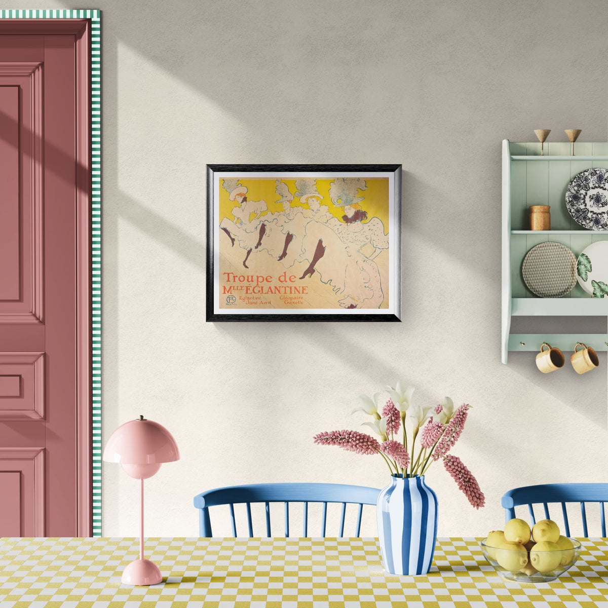 Dining room with a framed poster on the wall, table with flowers and fruit, and shelves with decorative items.