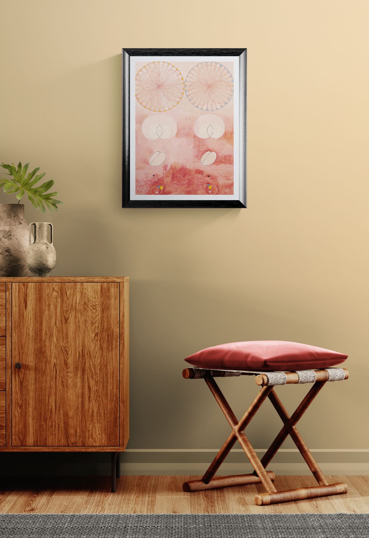 Framed artwork on a wall above a wooden cabinet and stool with a red cushion.