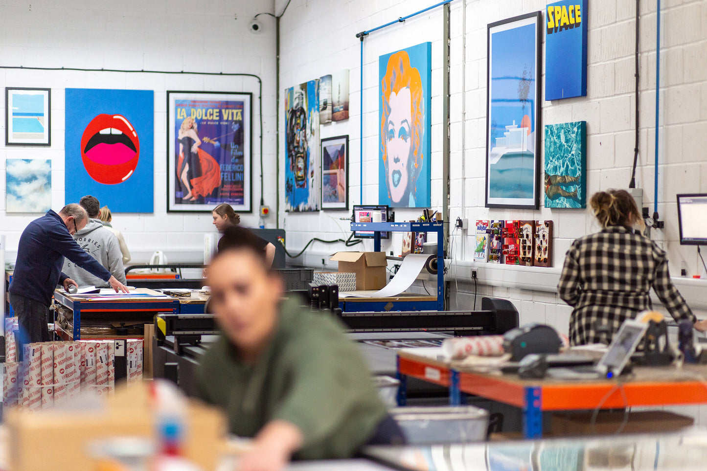Art studio with people working on prints and posters, featuring colorful artwork on the walls.