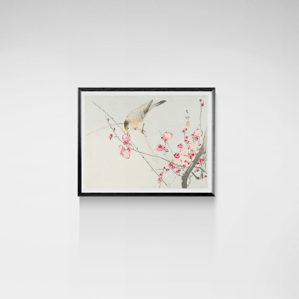 Framed artwork of a bird on a branch with pink flowers on a white wall.