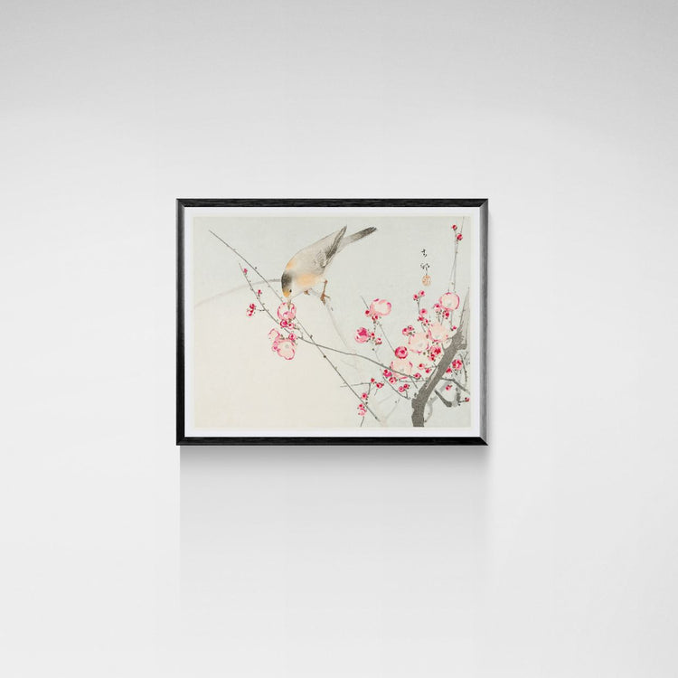Framed artwork of a bird on a branch with pink flowers on a white wall.