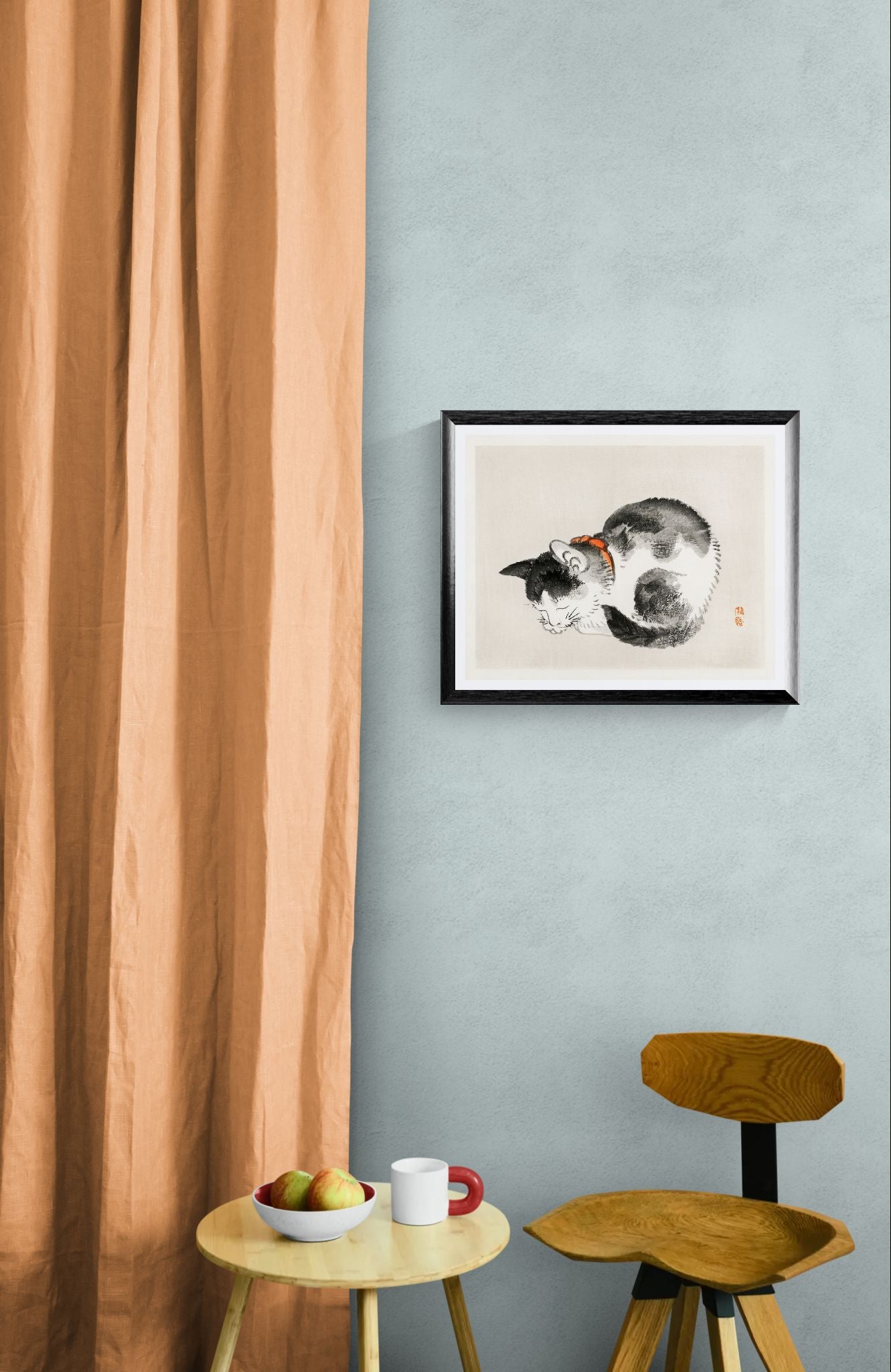Framed artwork of a cat on a light blue wall with a wooden chair and small table below.