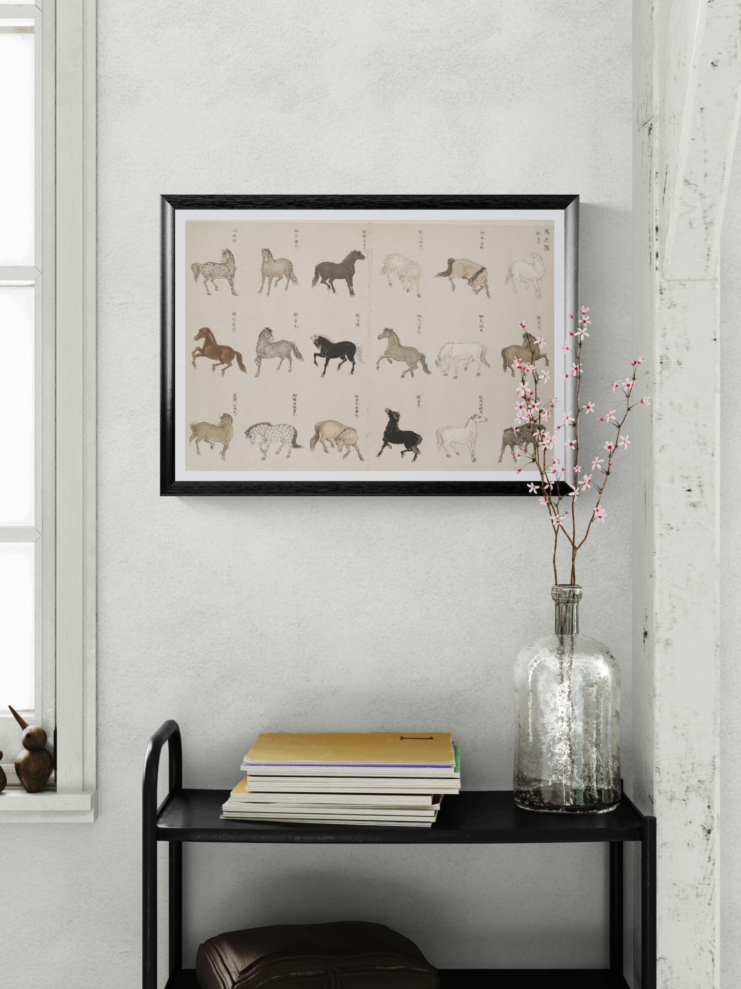 Framed artwork of horse illustrations on a wall with a vase and books on a shelf below.