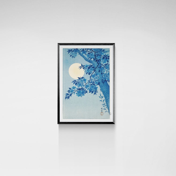 Framed artwork of a blue floral design with a moon on a white wall