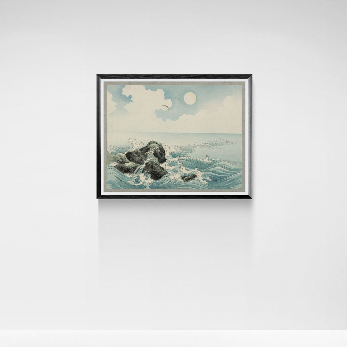 Framed artwork of a coastal scene with rocks and waves on a white wall.