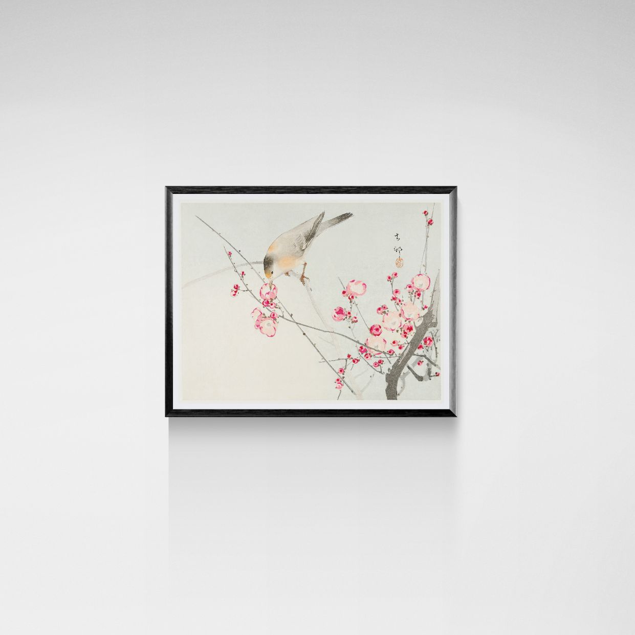 Framed artwork of a bird on a branch with pink flowers on a white wall.