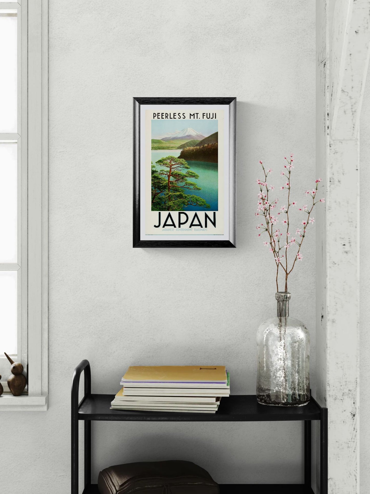 Framed poster of Mount Fuji with 'Japan' text on a wall above a black shelf.
