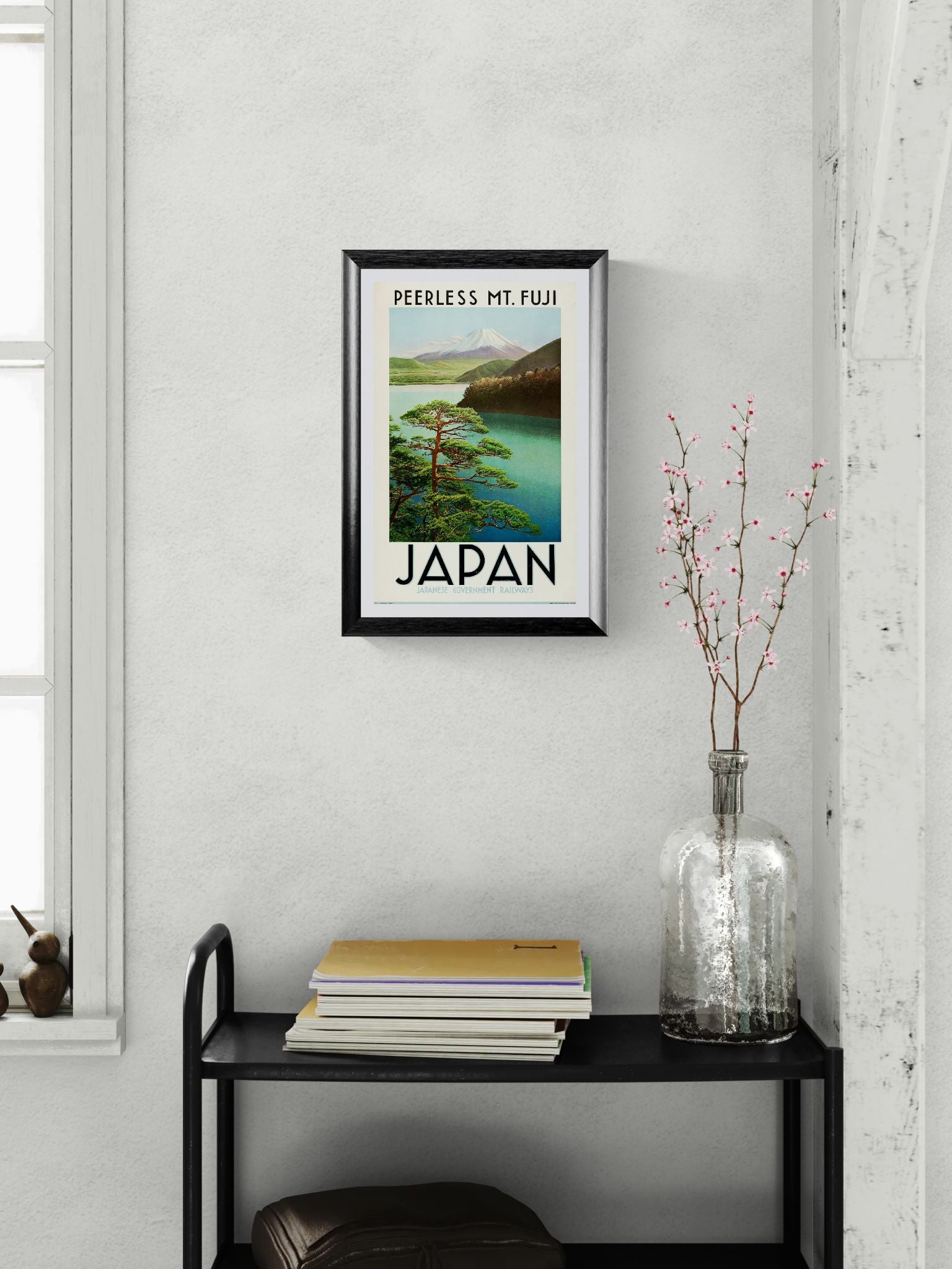 Framed poster of Mount Fuji with 'Japan' text on a wall above a black shelf.