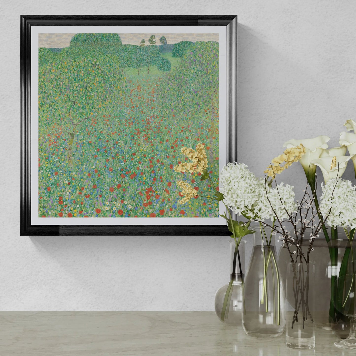 Framed artwork of a landscape with flowers on a wall above a table with floral arrangements.