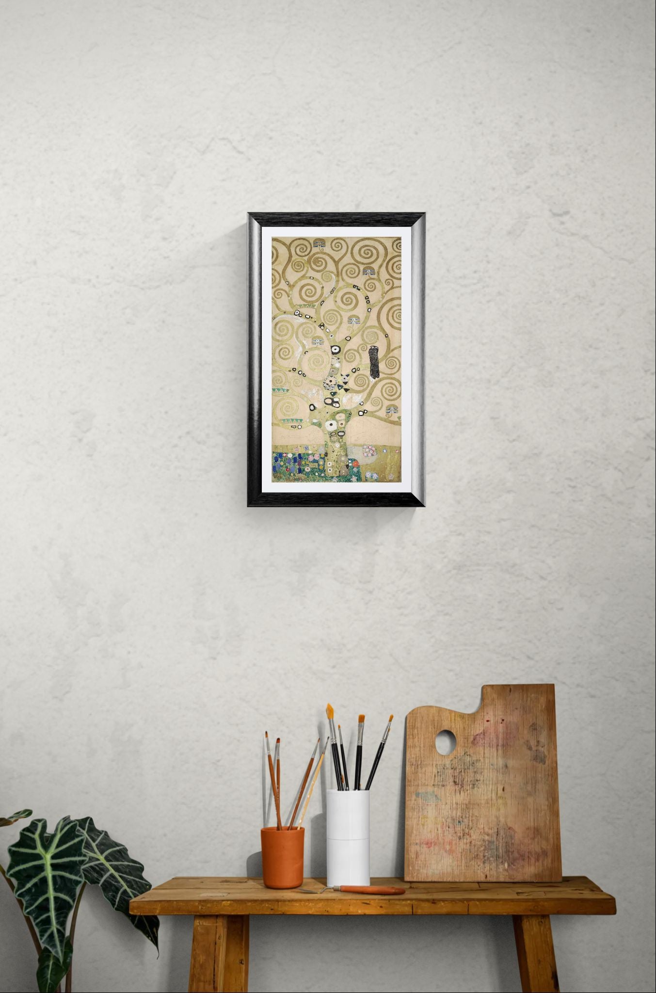 Framed artwork on a wall above a wooden table with art supplies.