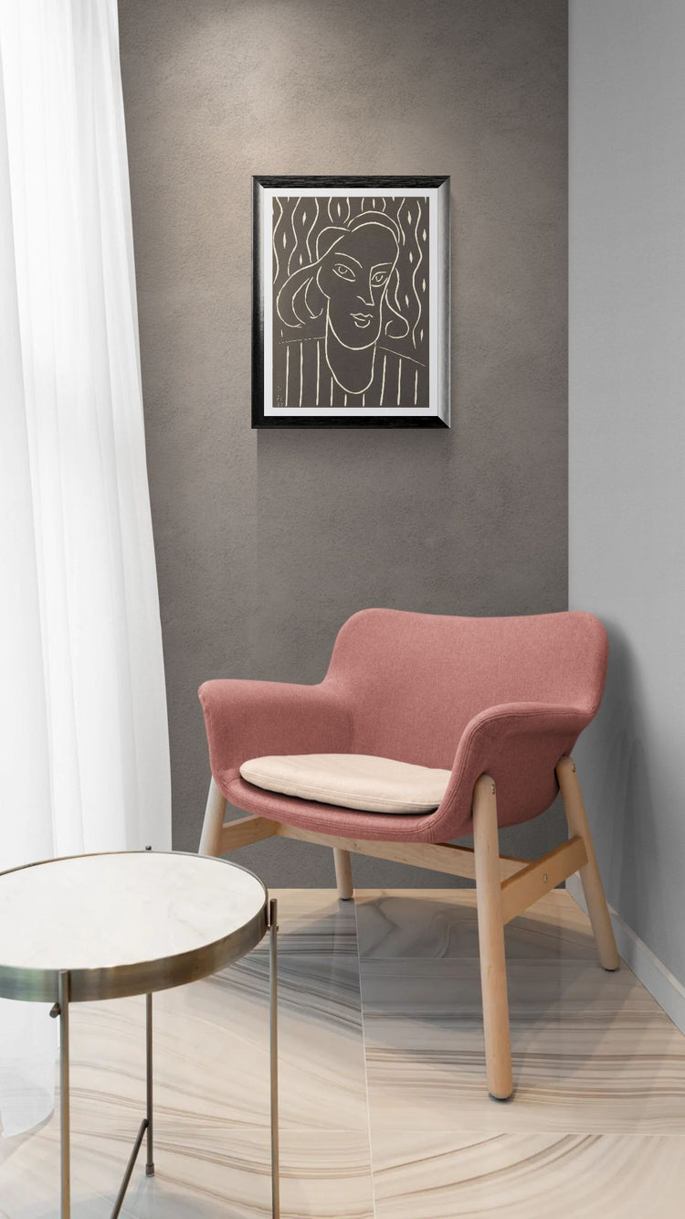 Pink armchair with a beige cushion in a room with a framed artwork on the wall.