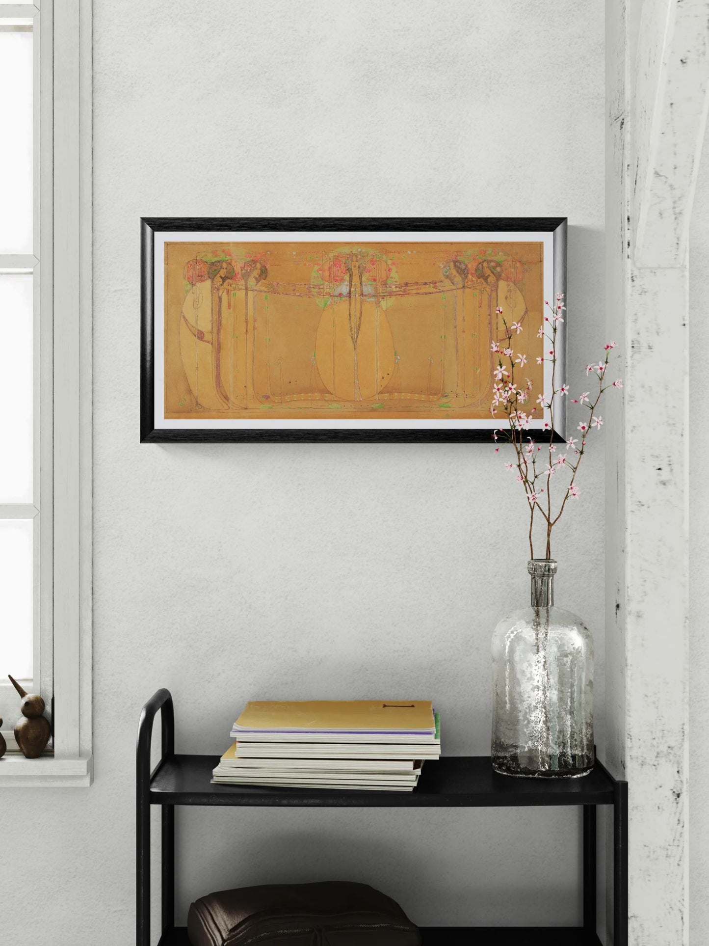 Framed artwork on a wall above a black shelf with books and a vase.