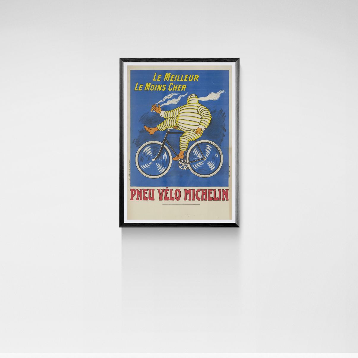 Framed poster of Bibendum riding a bicycle with Michelin tire advertisement on a white wall.