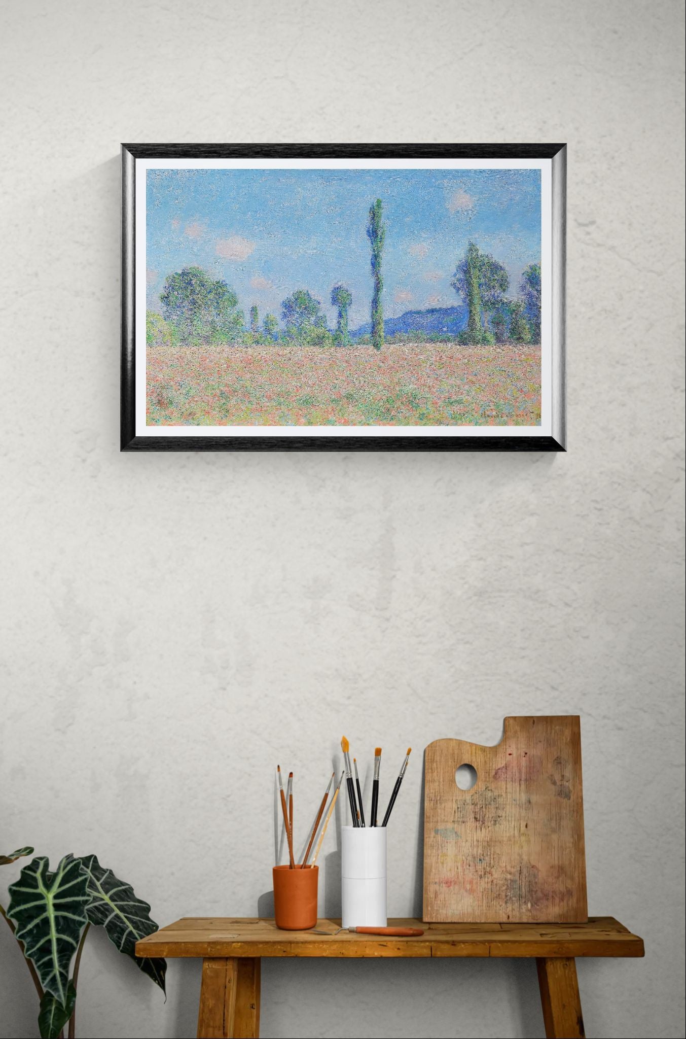 Framed painting of a landscape on a wall above a wooden table with art supplies.