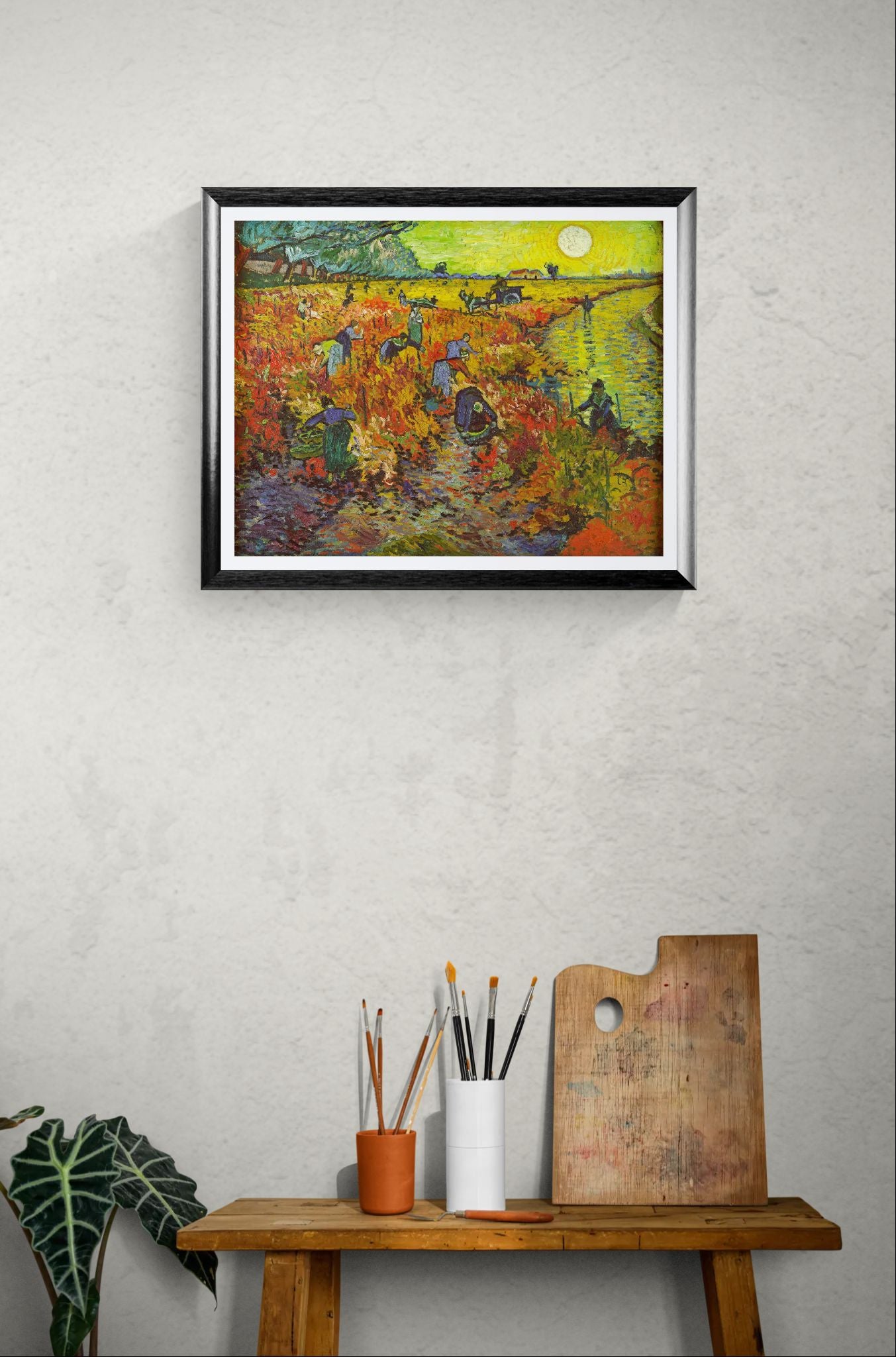Framed painting of a colorful landscape on a wall above a wooden table with art supplies.