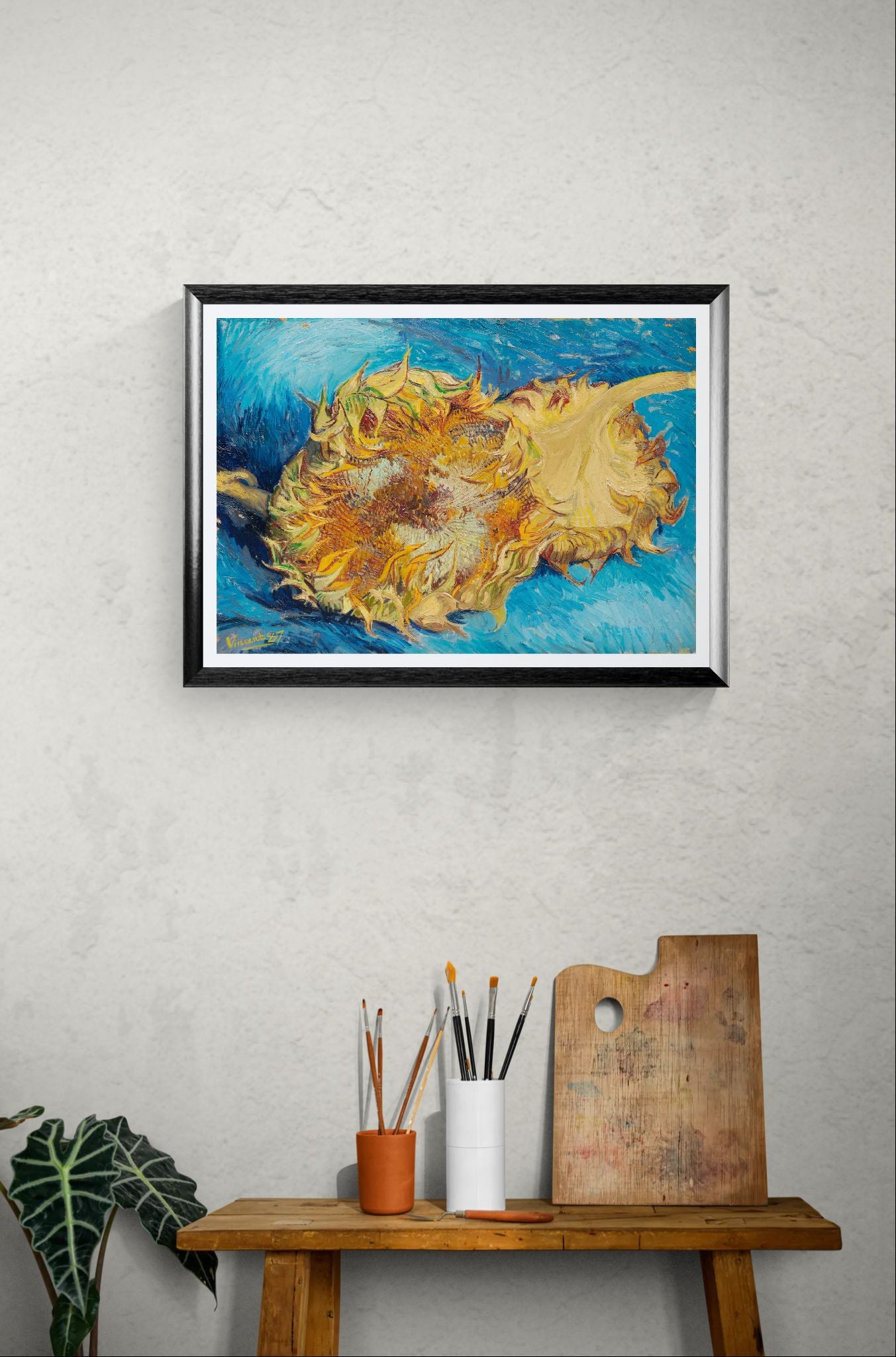 Framed artwork of sunflowers on a wall above a wooden table with art supplies.