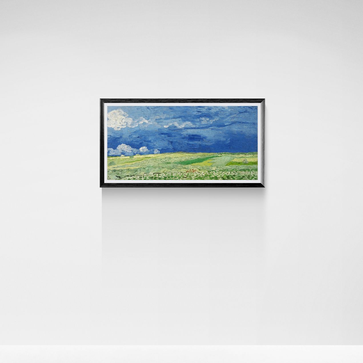 Framed painting of a landscape with green fields and blue sky on a white wall.