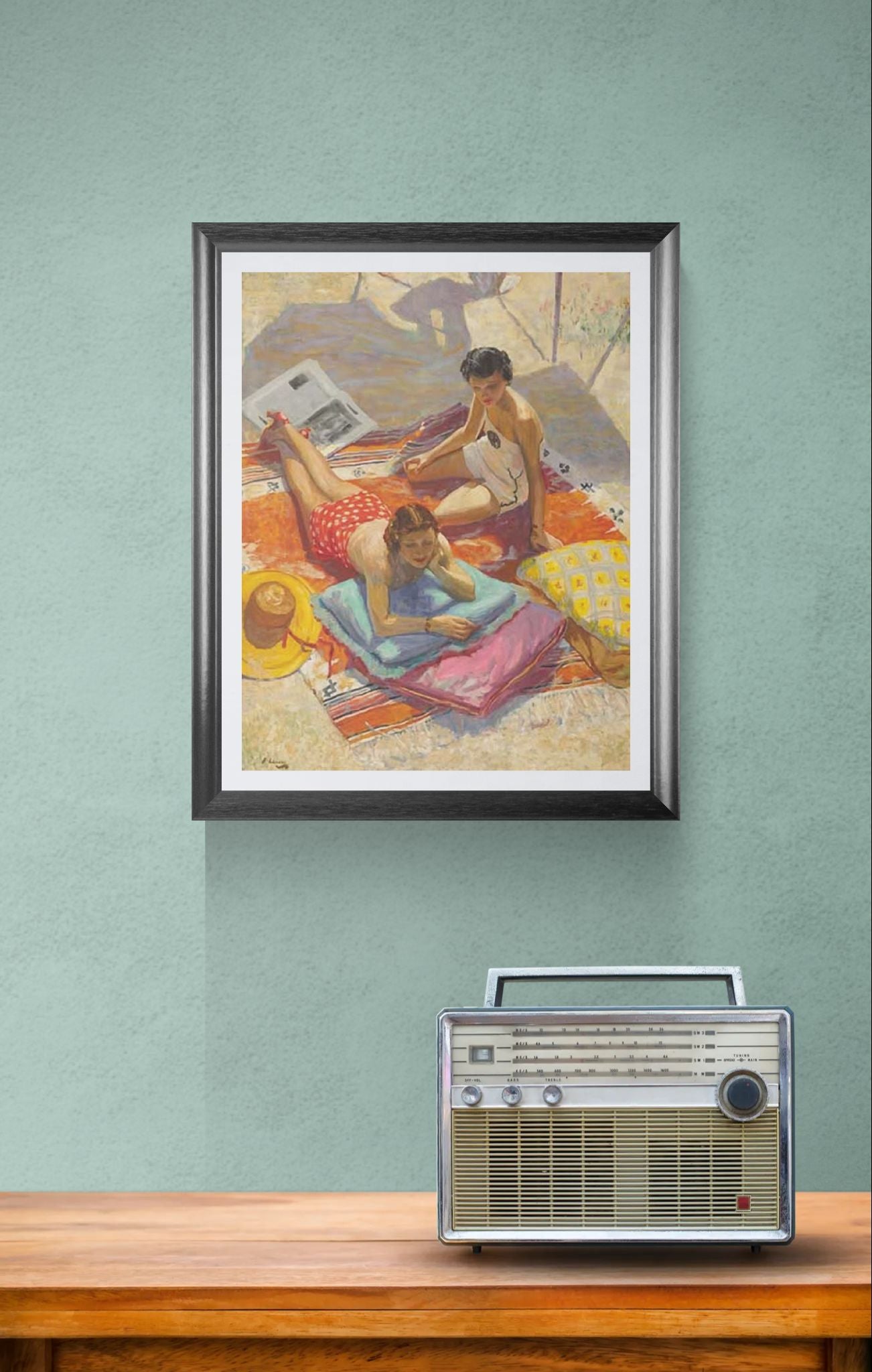 Framed artwork of a beach scene with two people on a towel, placed above a wooden surface with a vintage radio.