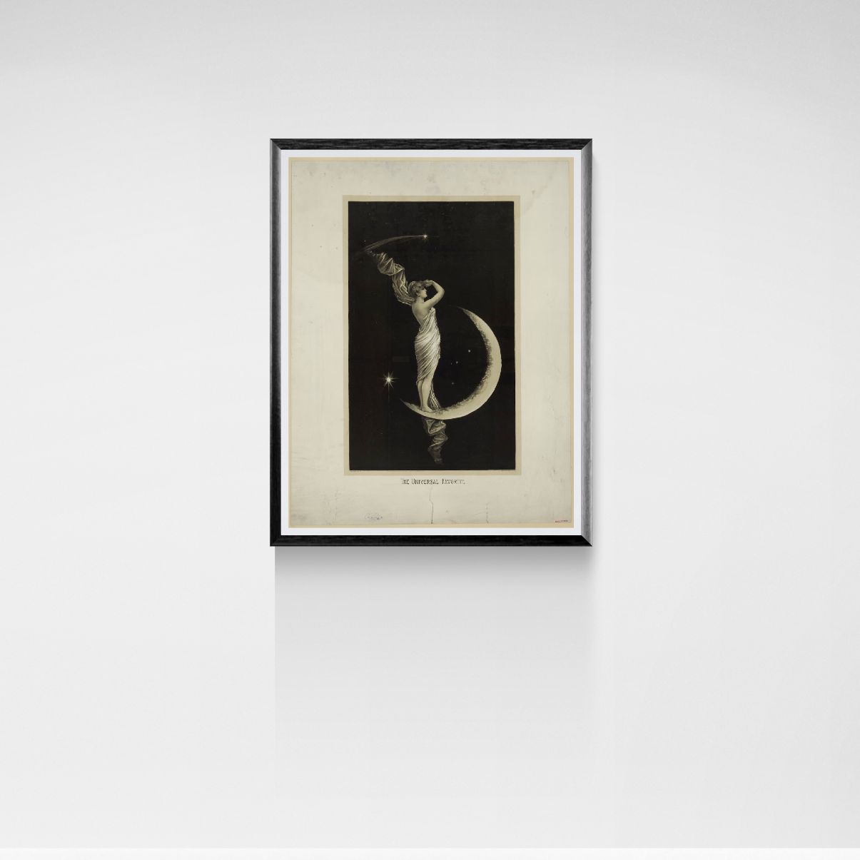 Framed black and white print of a woman on a crescent moon against a white wall.
