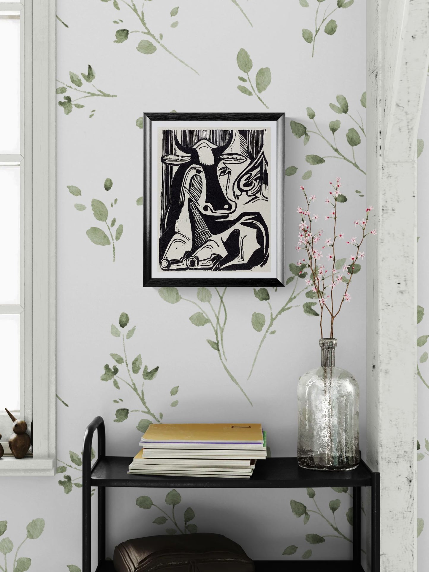 Framed artwork on a wall with decorative leaves and a vase below