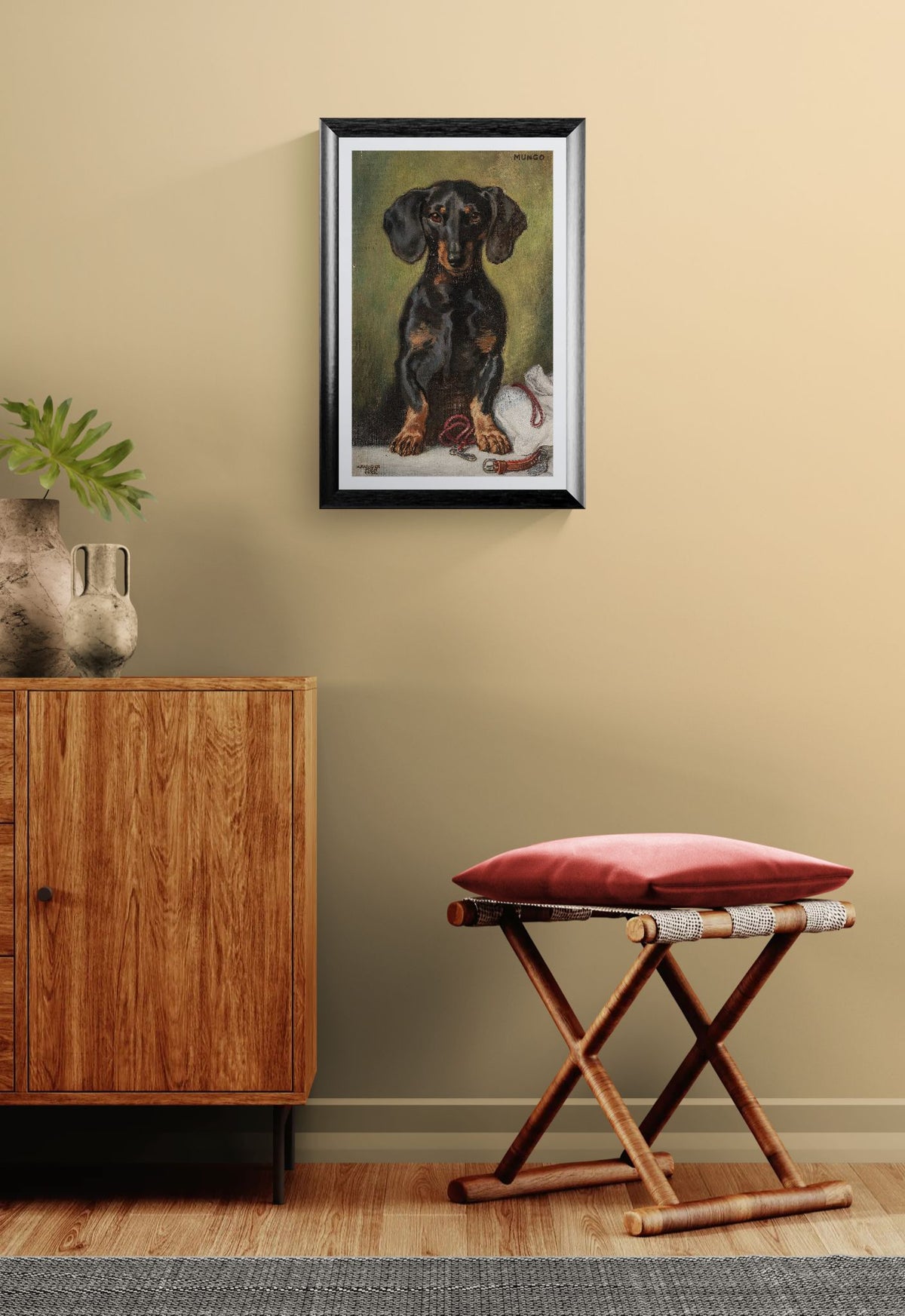 Framed artwork of a dog on a wall above a wooden cabinet and stool with a red cushion.