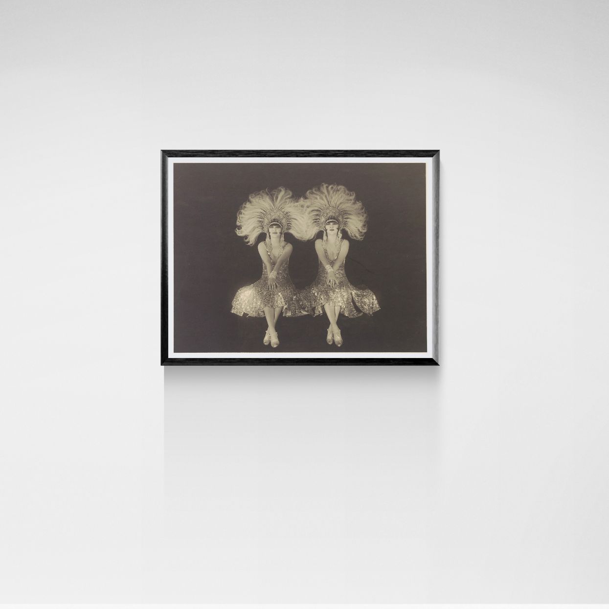 Framed artwork of two dancers with plumes on a white wall