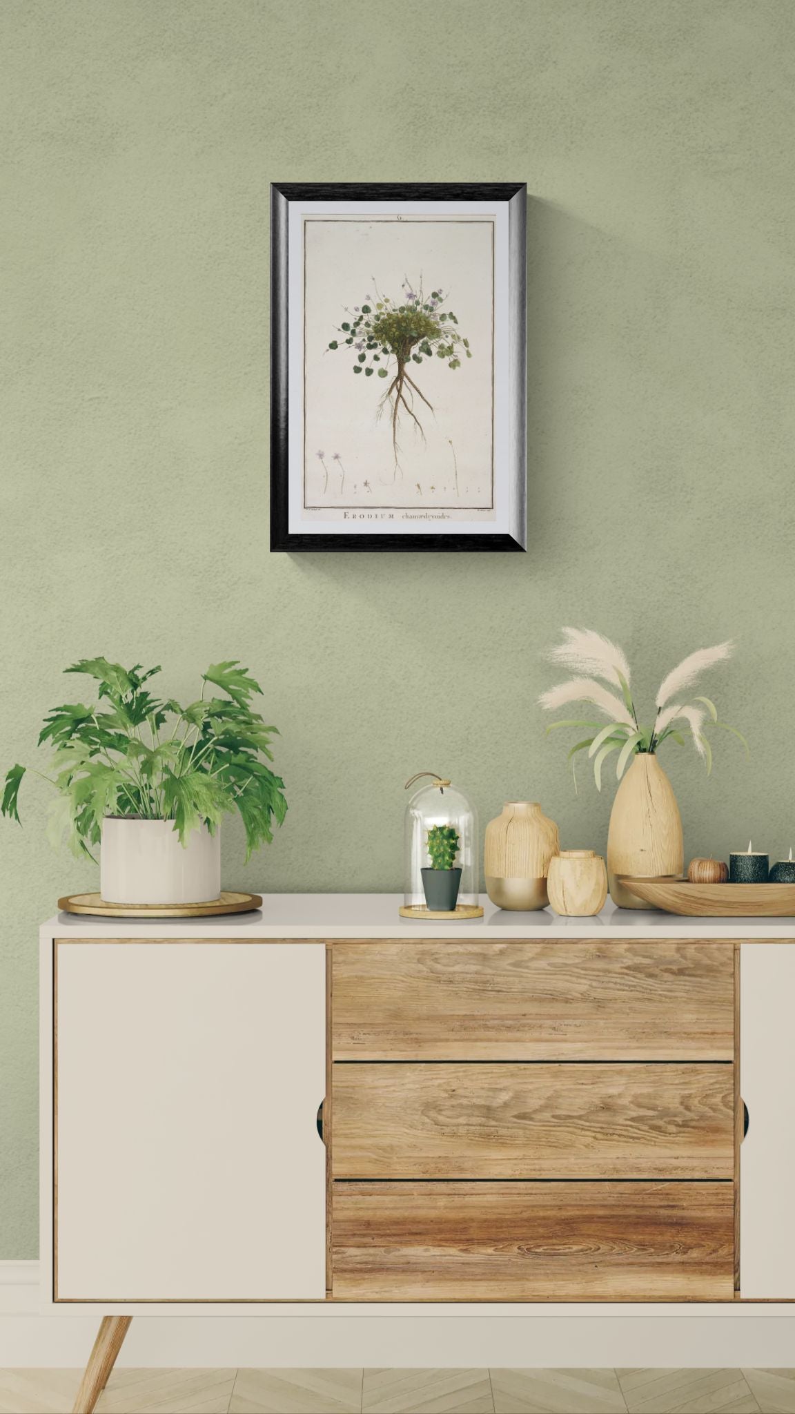 Decorative setup with a framed plant print, potted plants, and vases on a wooden cabinet against a green wall.
