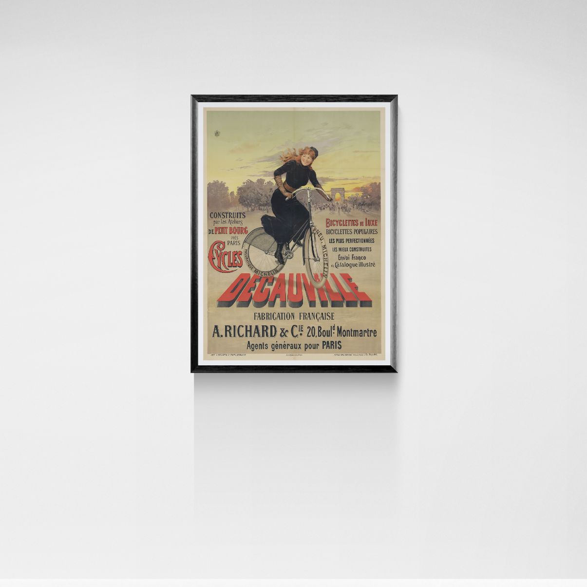 Framed vintage poster of a woman riding a bicycle on a white wall