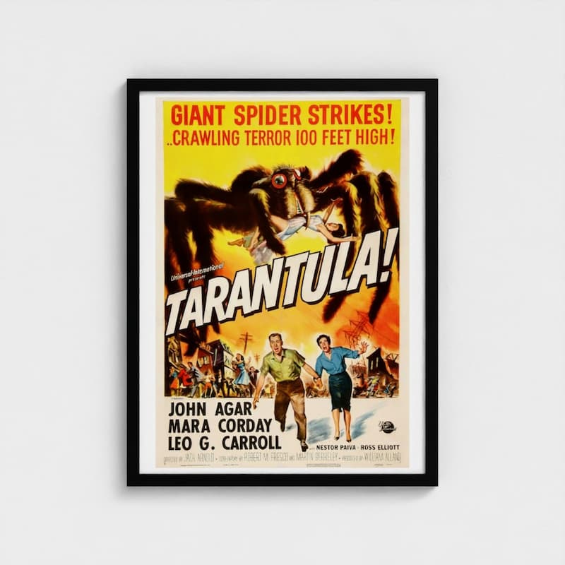 A framed vintage movie poster for the 1956 film 'Tarantula!' featuring a giant spider, bold yellow title text, and illustrated characters at the bottom, displayed against a light gray wall.