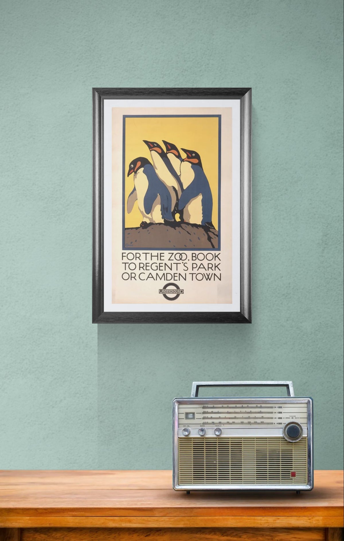 Framed poster of penguins on a green wall with a vintage radio below.