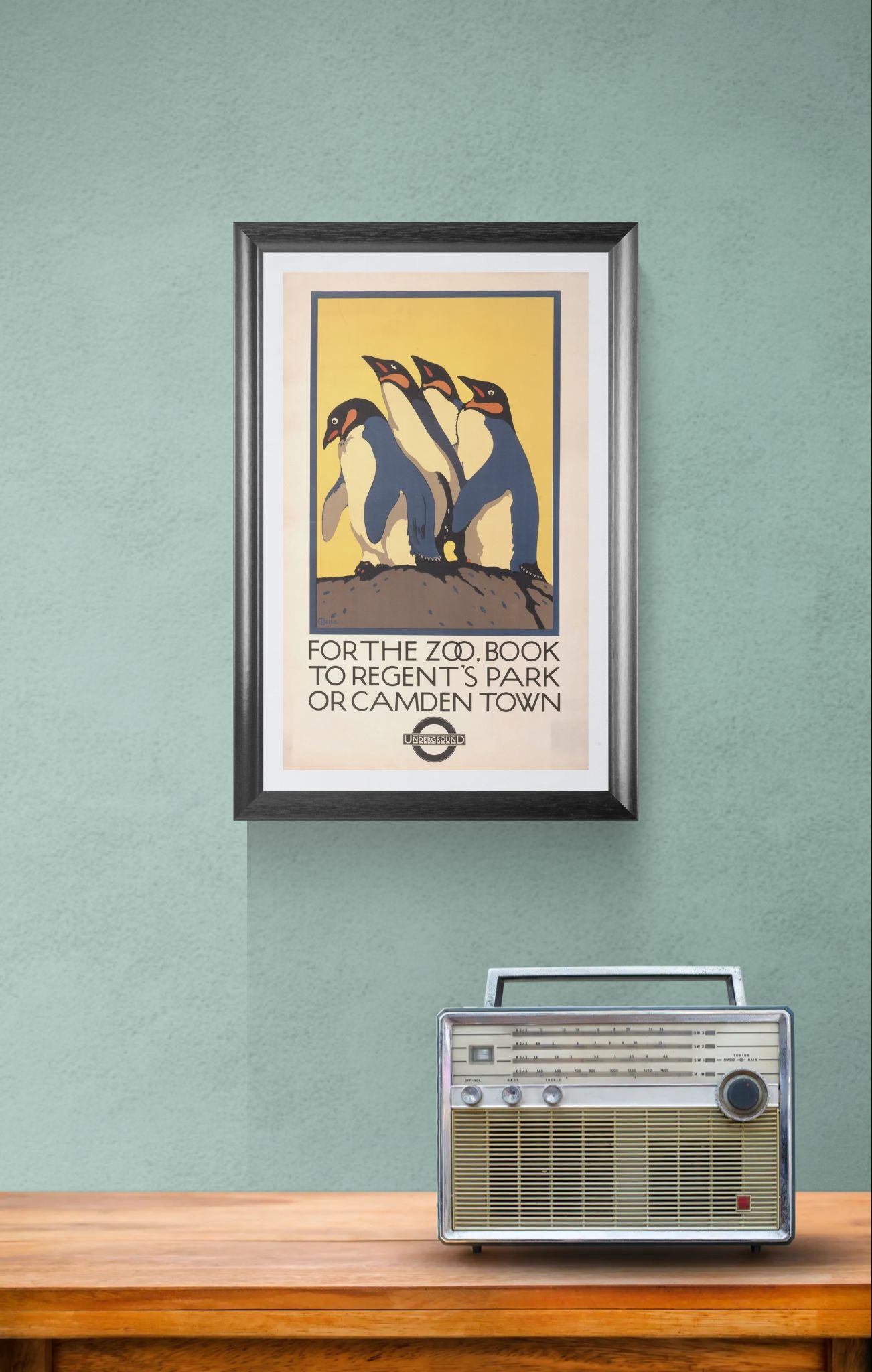 Framed poster of penguins on a green wall with a vintage radio below.