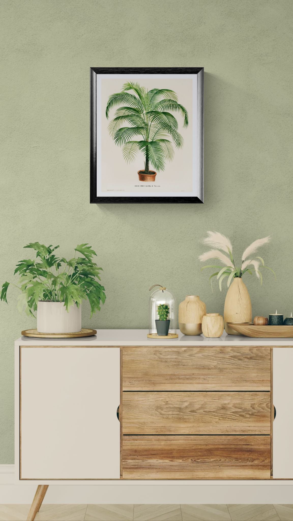 Decorative setup with a framed plant print, potted plants, and vases on a wooden cabinet against a green wall.