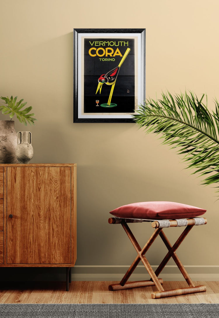 Framed Cora Vermouth advertisement on a wall with a wooden cabinet and stool in a room.