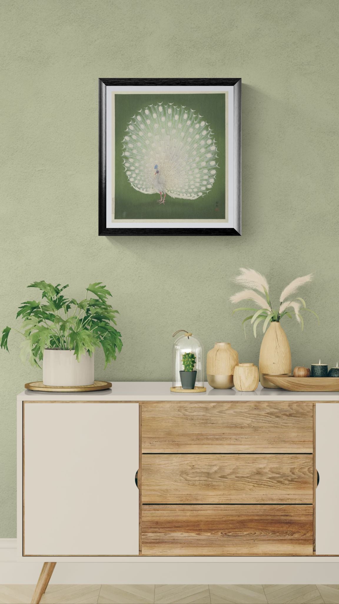Decorative setup with a framed artwork of a peacock, plants, and a wooden cabinet against a green wall.