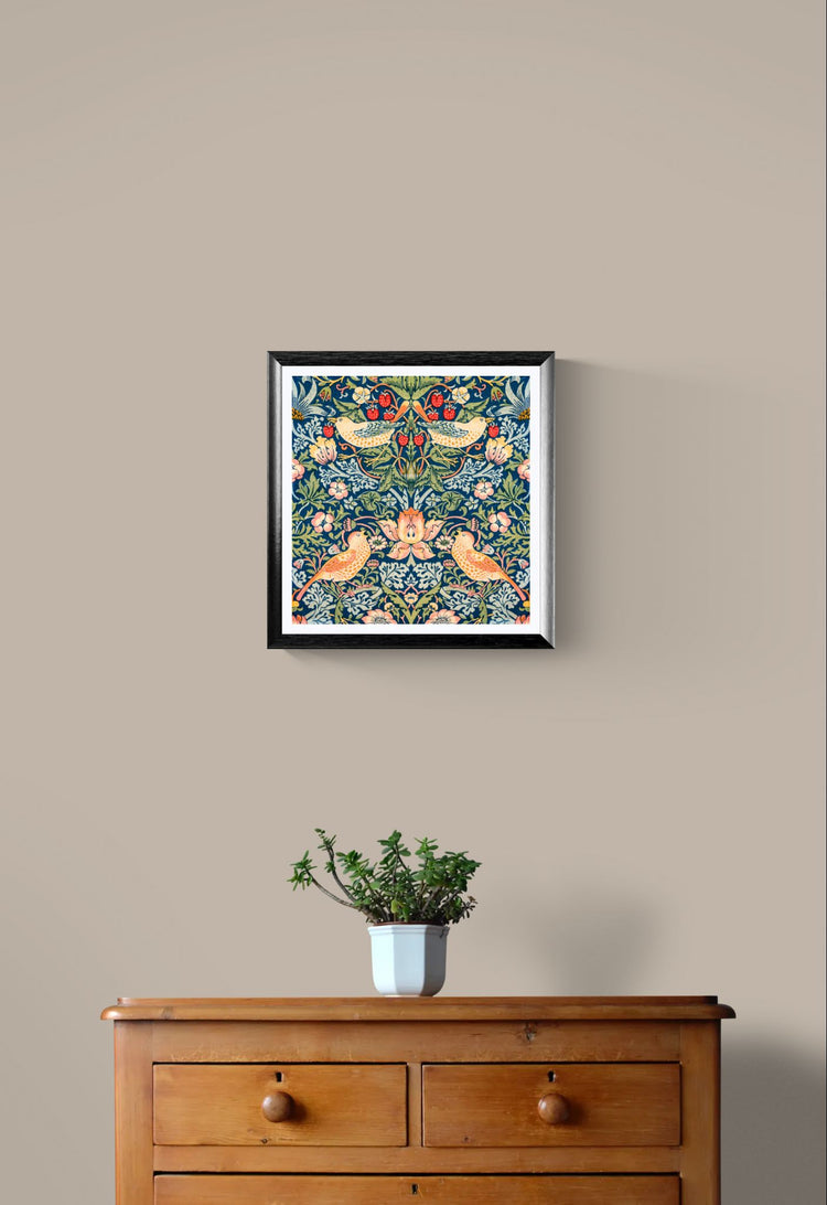 Framed artwork with floral and bird design on a beige wall above a wooden dresser with a plant.